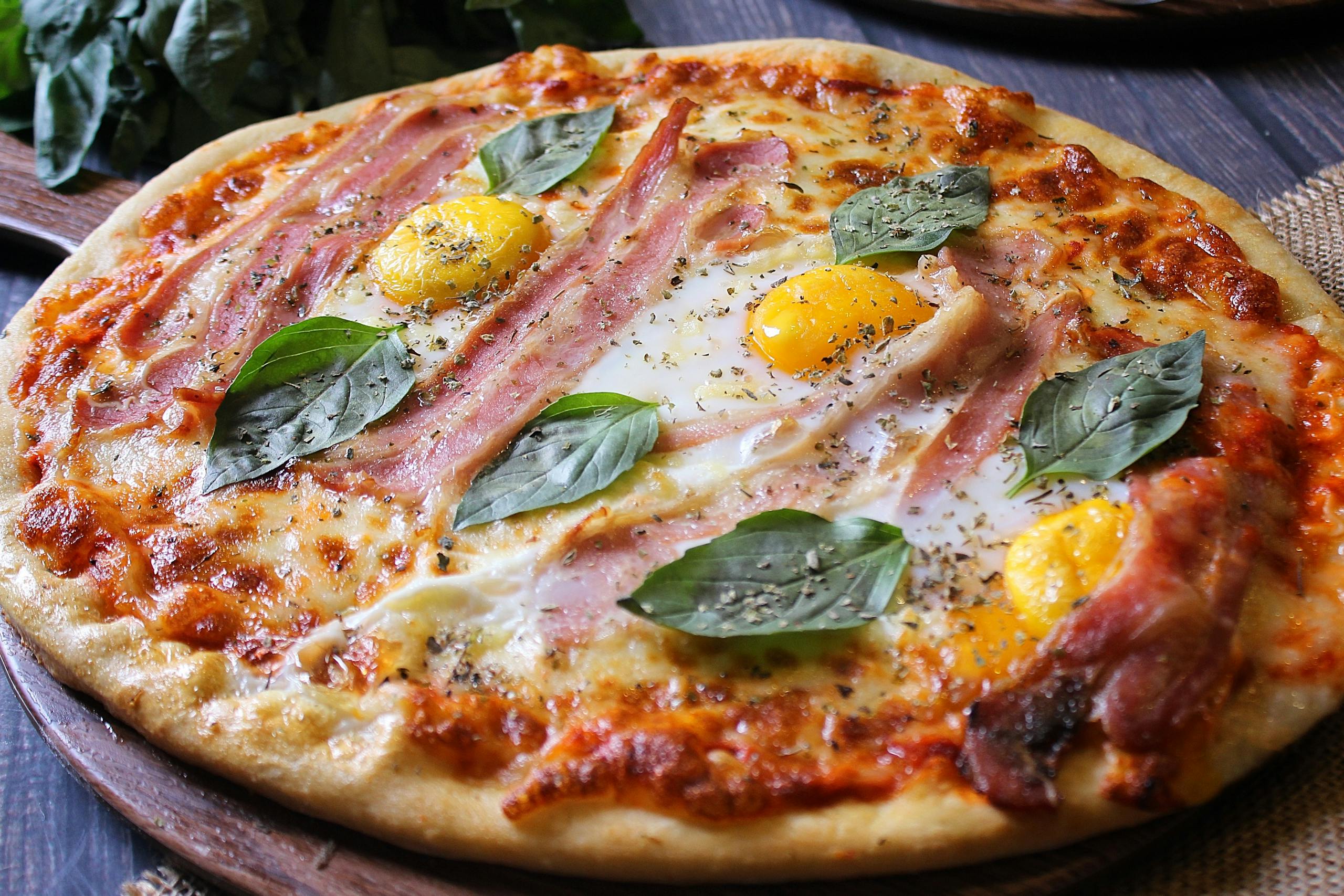 Delicious gourmet pizza topped with ham, eggs, and fresh basil leaves, perfect for a culinary delight.