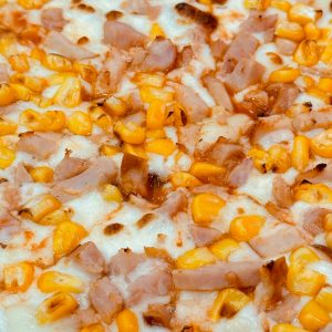 Mouth-watering close-up of a corn and ham pizza slice with melted cheese.